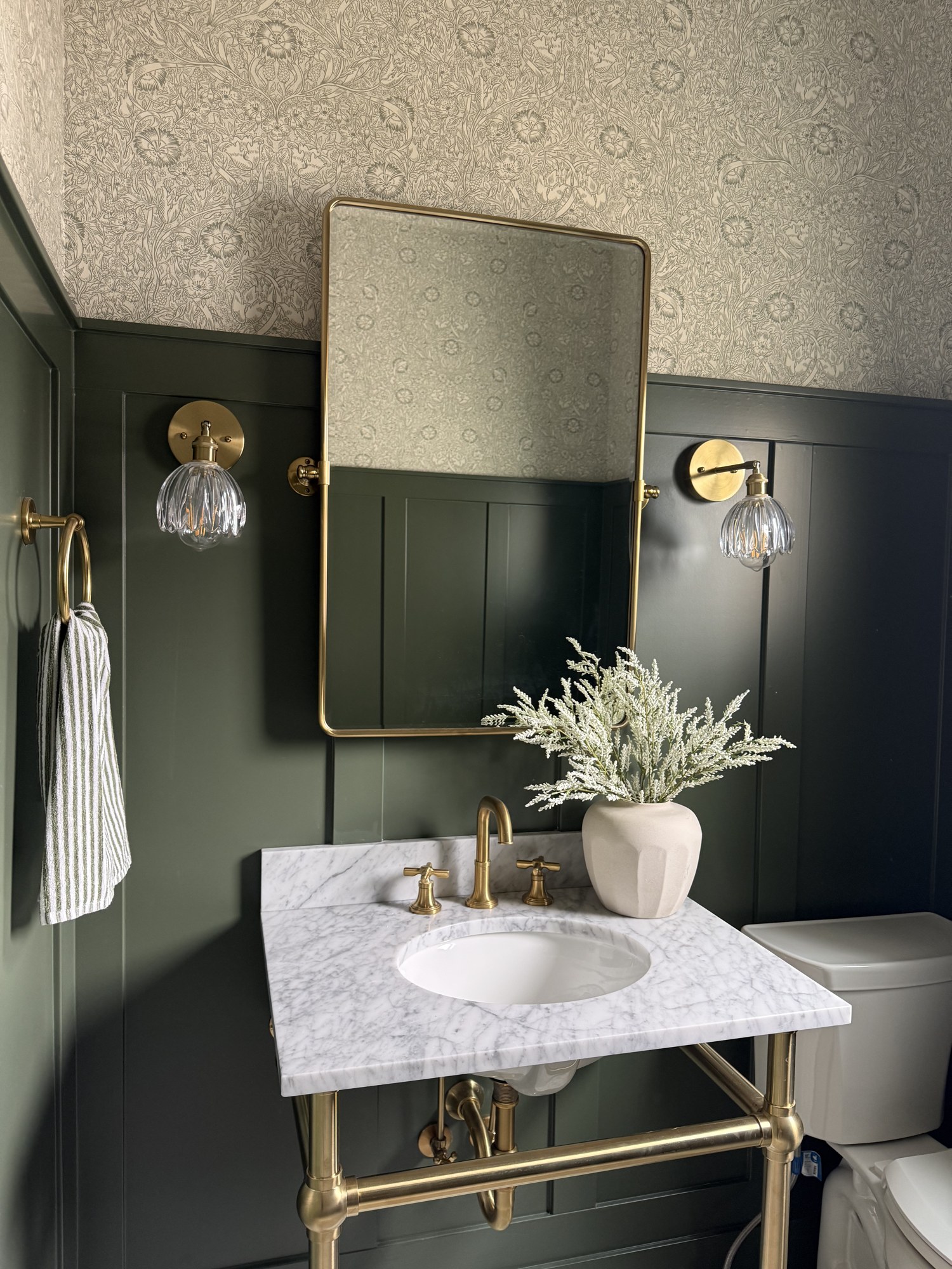 Wide view of a Middleton bathroom with a marble vanity, brass fixtures, patterned wallpaper, and dark wall paneling